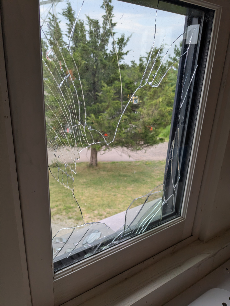 Spiderweb crack pattern across a windowpane with trees visible outside